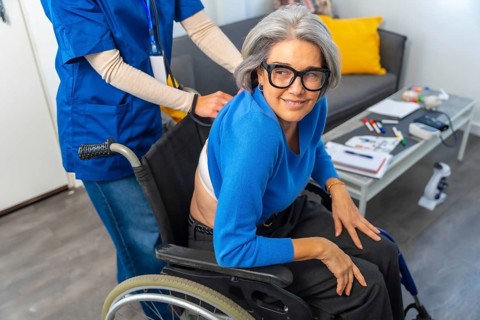 Senior woman in a wheelchair smiling and looking at camera while a professional nurse or caregiver
