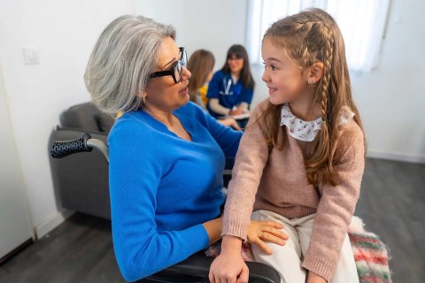 Grandma in a wheelchair interacting happily with her granddaughter, sharing a warm moment during a