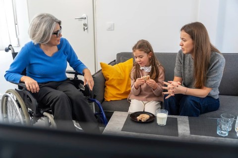 Grandmother in a wheelchair interacting with her family, including a young girl eating a snack and