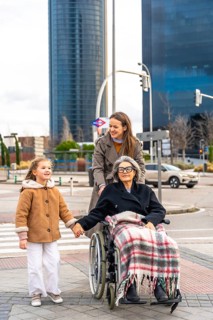 Three generations family, including little girl holding hands with her grandmother in a wheelchair,