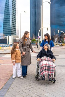 Family members and a caregiver are walking with an elderly woman in a wheelchair, providing care