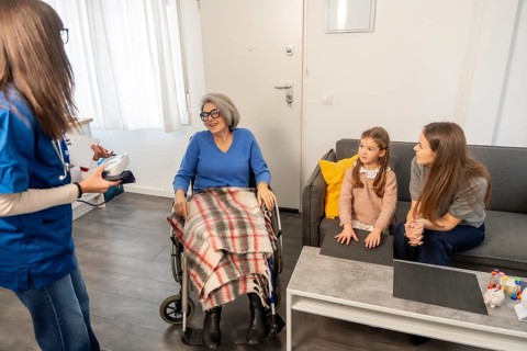 Nurse communicating with an elderly woman in a wheelchair, while her daughter and granddaughter are