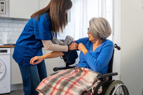 Healthcare professional in blue scrubs measuring an elderly woman's blood pressure in a wheelchair