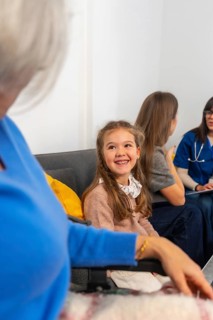 Smiling young girl visits grandmother in a wheelchair at a nursing home, surrounded by family and a