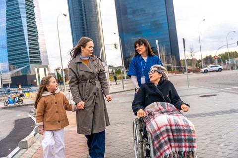 Family members and a caregiver pushing an elderly woman in a wheelchair, leaving a healthcare