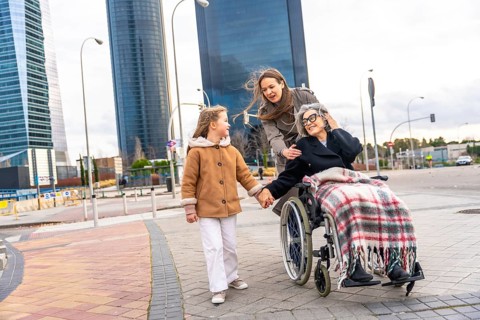 Multi generational women sharing a city walk, grandmother in wheelchair holding granddaughter's