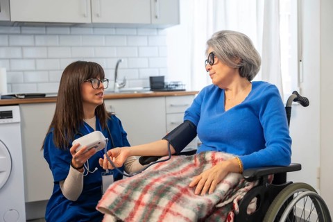 Healthcare professional assisting an elderly woman in a wheelchair by measuring her blood pressure