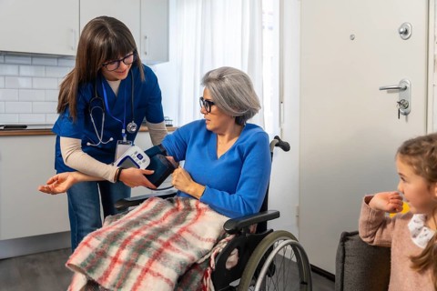 Healthcare professional assisting an elderly woman in a wheelchair by measuring her blood pressure