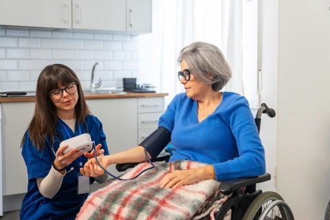Nurse using a digital device to check blood pressure on arm of an elderly woman seated in a