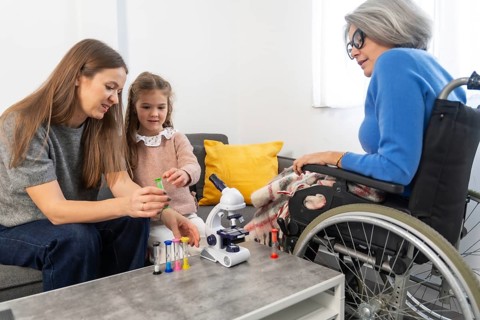 Granddaughter and mother playing with a microscope and colorful hourglasses at home while a senior