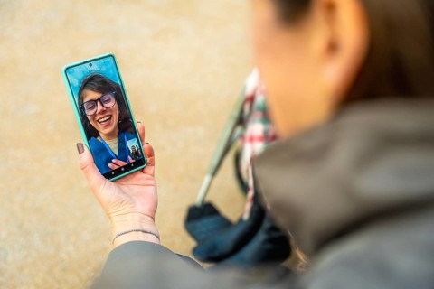 Person holding smartphone showing video call with smiling woman while pushing a wheelchair