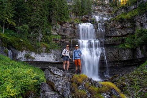 Two hikers standing on rocks in front of Cascata di Mezzo waterfall, long exposure, Vallesinella,