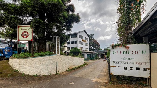 Entrance area of a facility with signs, trees and cloudy sky, tea factory in the mountains near