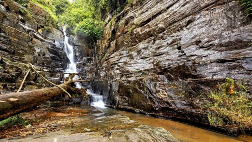 A narrow waterfall flows in a rough environment from rocks surrounded by forest, waterfall in the