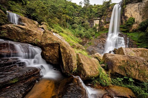 Two waterfalls flow between large rocks in a lush, green jungle, waterfall in the mountains of