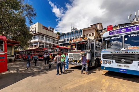 People gather under clear skies at a bus stop surrounded by buses, Kandy bus station in Sri Lanka