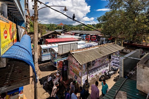 View of a depot densely staffed by buses, surrounded by billboards and trees, Kandy bus station in