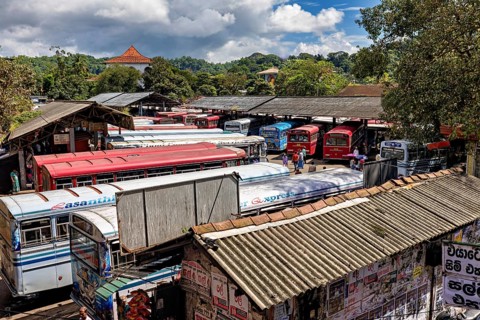 View of a bus depot with numerous parked buses and green hills in the background, Kandy bus station