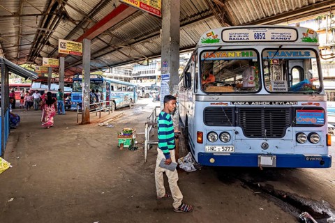 A bus station with parked buses and people walking between the covered stops, Kandy bus station in