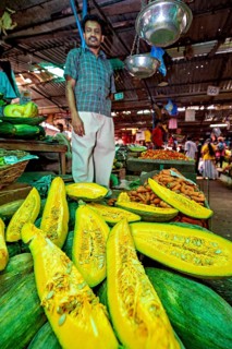 A man stands at a market stall with glowing pumpkin and other fresh vegetables, The old market