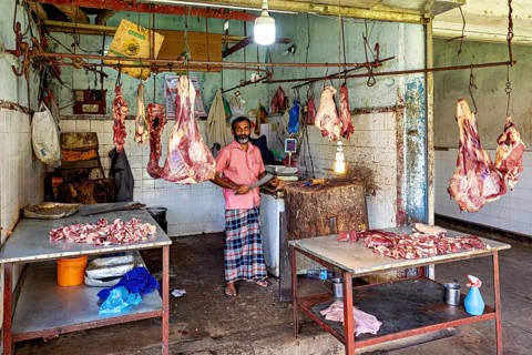 Butcher in traditional slaughterhouse with pieces of meat hanging on hooks, The old market halls of