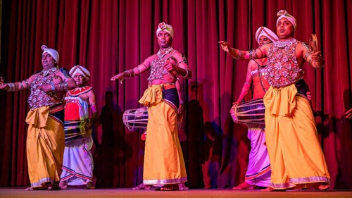 Men in traditional clothing play drums on a stage in front of a red curtain, folklore and dancers
