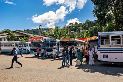 Buses park at a stop under tropical skies as people walk around, Kandy bus station in Sri Lanka