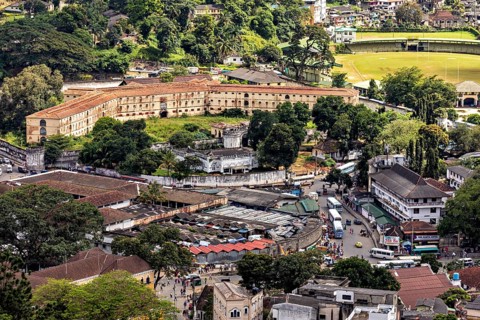 View of a historic fortress next to a lawn surrounded by city and trees, view of the city center of