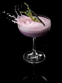 An ice cube cube falls into a cocktail cup and allows the liquid to splash on, studio shot against