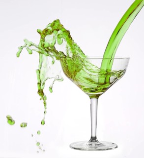 A powerful flood of green liquid pours into a cocktail glass and spills over, studio shot against a