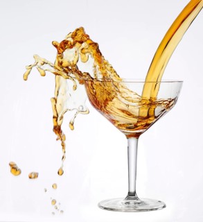 A strong flood of golden yellow liquid pours into a cocktail glass and spills over, studio shot