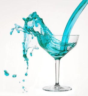 A powerful flood of blue liquid pours into a cocktail glass and spills over, studio shot against a