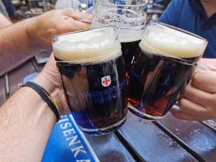 Three people toast in a beer garden with dark beer glasses, cheerful atmosphere, Weltenburg Abbey,
