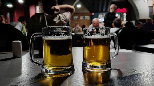 Two beer glasses on a table in a bar with people in the background at dusk, Georgia