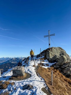 Hiker next to summit cross at summit of Feldalphorn, winter hiking, Kitzbühel Alps, Tyrol, Austria