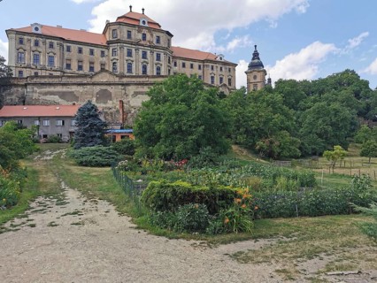 View of a monastery, castle with garden in the foreground, surrounded by lush vegetation on a