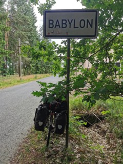 Bicycle with luggage bags in front of a Babylon town sign on a road through the forest, Czech