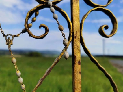 Close-up of a metal religious ornament, part of a cross, with a meadow and sky in the background,