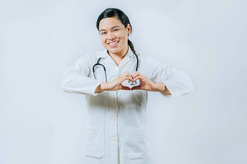 Smiling asian female doctor making heart shape isolated. Asian healthcare worker gesturing heart