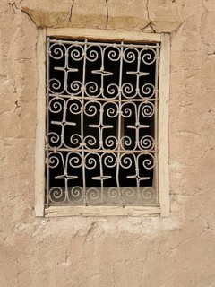 Decorated window screen in a crumbling, beige clay wall with rustic ambiance, Morocco