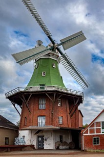 Historic brick windmill with green roof under cloudy sky, An old historic windmill near Stade