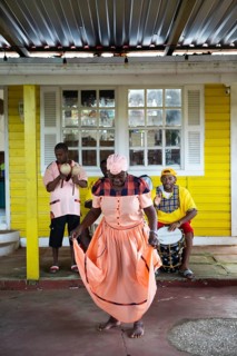 Guatemalan woman in traditional dress singing and dancing, men playing music in the back, Garifuna