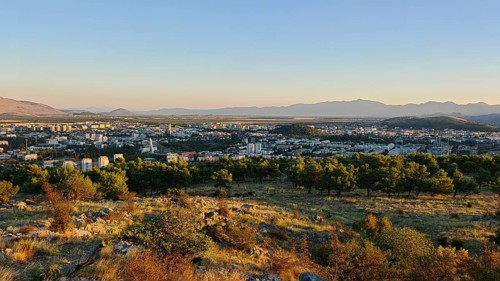 A city surrounded by nature with trees in the foreground and mountains in the background,