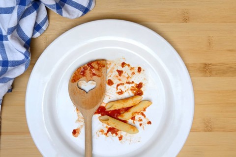 Plate with cooking spoon and leftovers from pasta, food waste