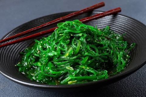 Chuka salad, made from fresh seaweed, with sesame dressing, served in a black bowl, with chopsticks