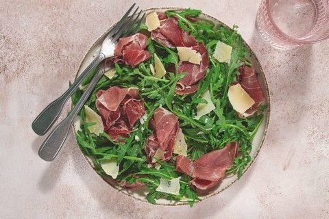 Fresh arugula salad with prosciutto and grated parmesan cheese, on a plate, homemade, no people
