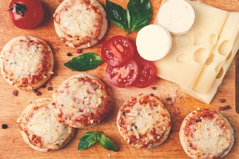 Freshly baked mini pizza, on a wooden board, with fresh vegetables and cheese, top view