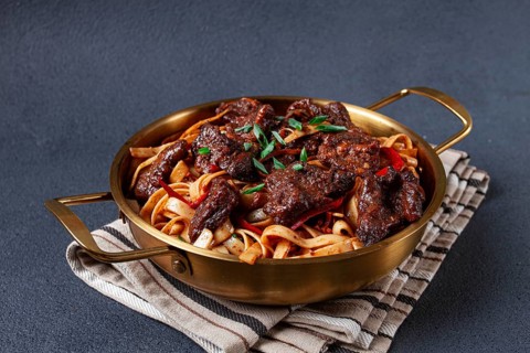 Udon noodles with Mongolian beef, green onions and vegetables, in a brass pan, on a gray