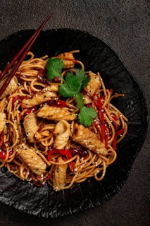 Udon noodles, with squid and vegetables, on a black plate, homemade, no people