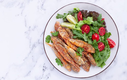 Fried crispy mullet fish, with fresh salad, on a plate with lime, no people